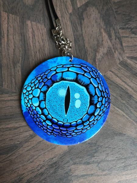 Collier breloque garçon rond bois modèle œil crocodile ou dragon fond bleu Comme un ange
