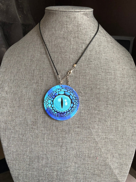Collier breloque garçon rond bois modèle œil crocodile ou dragon fond bleu Comme un ange