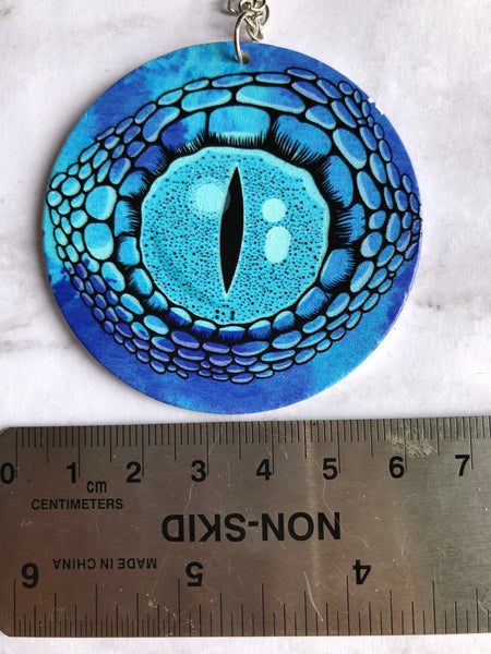 Collier breloque garçon rond bois modèle œil crocodile ou dragon fond bleu Comme un ange